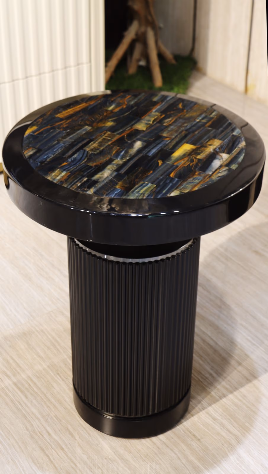 Round side table with a banded blue-brown tiger's eye stone top on a black fluted cylinder pedestal base.
