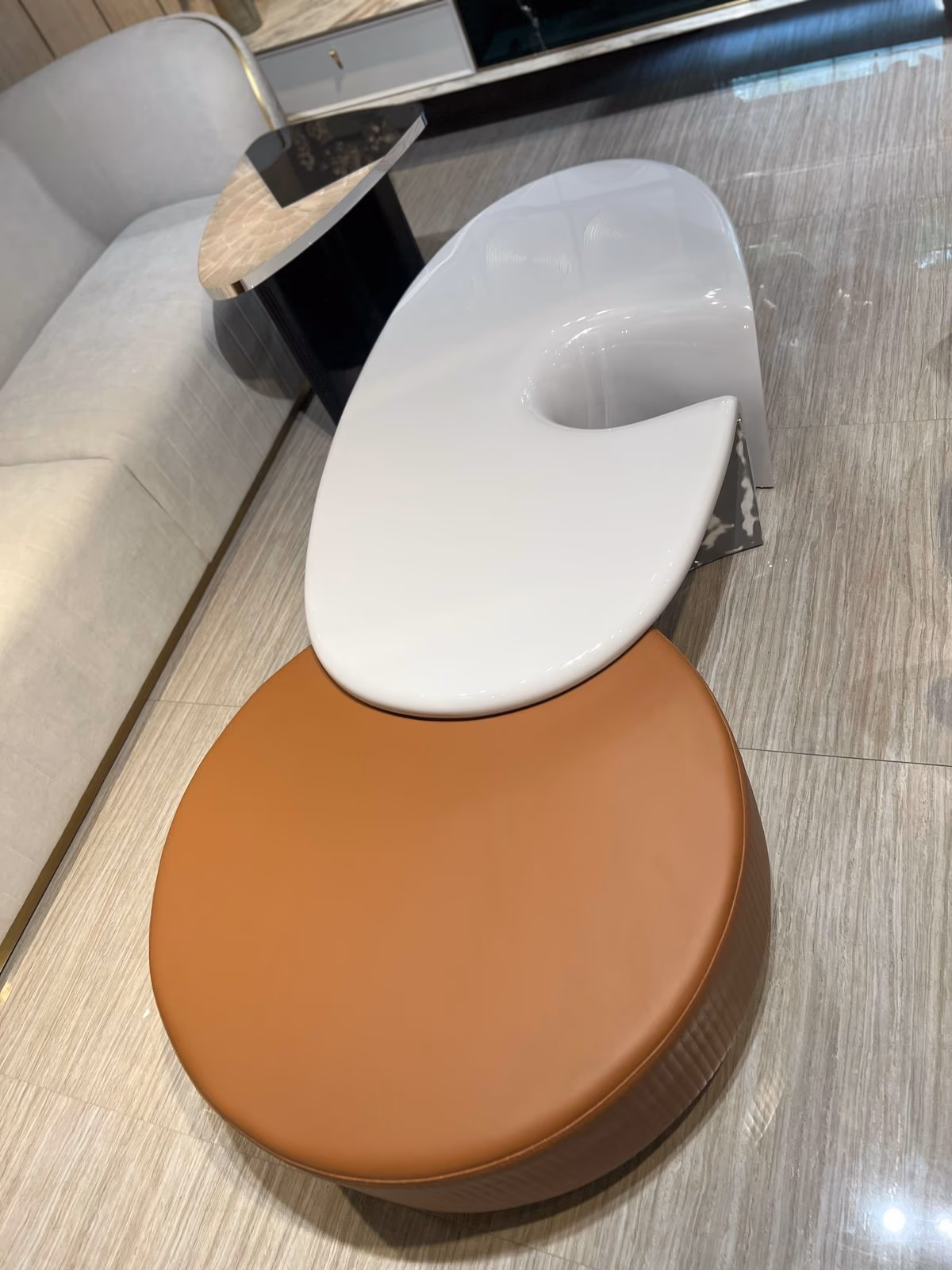 A glossy white organic-curved lacquer stool paired with a round cognac leather pouf with a pleated side band.
