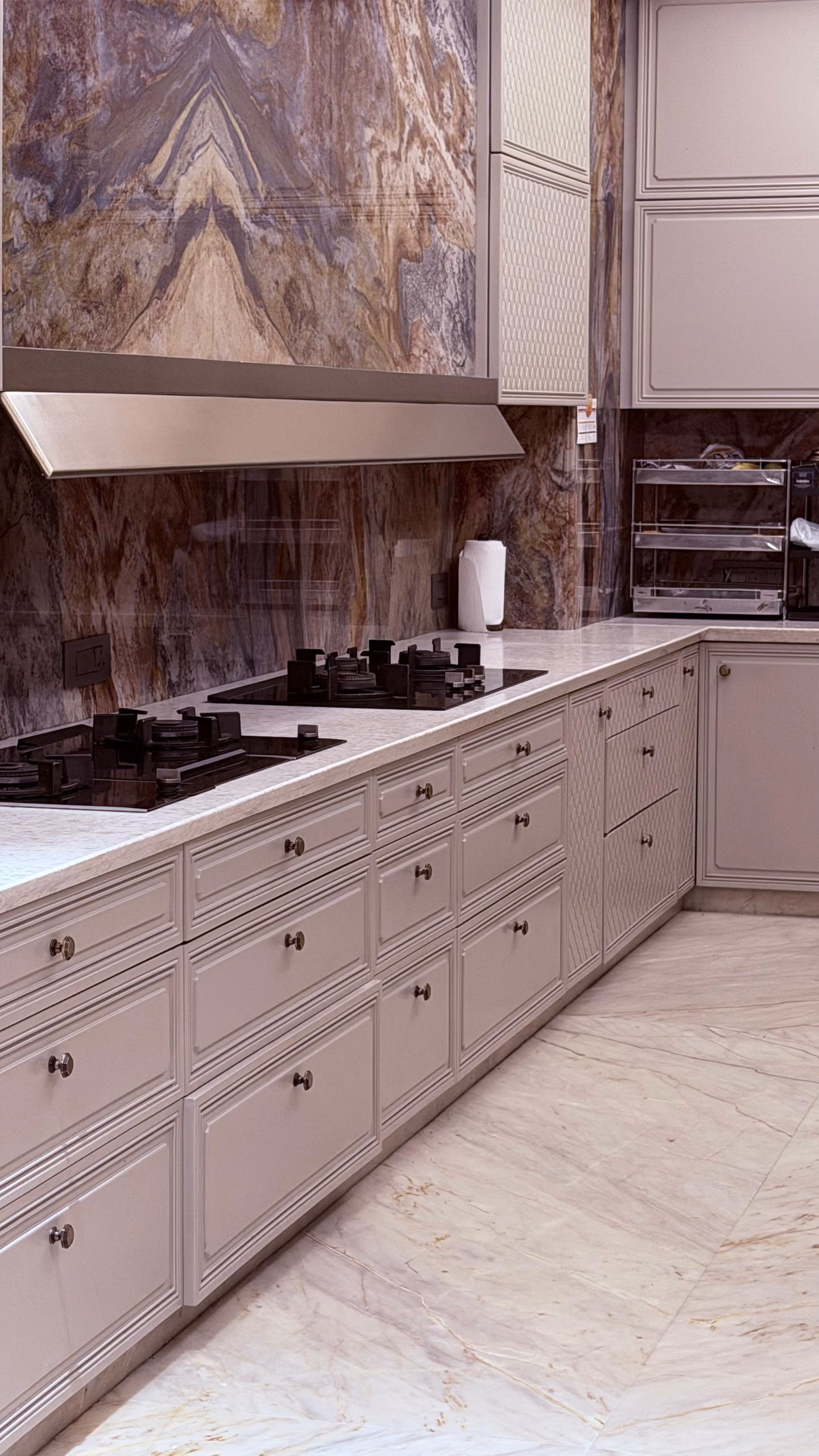 Close view of the modular kitchen's cooking run, with a black gas hob, slim chimney, brass-knobbed drawer banks and a swirling brown-and-blue marble backsplash.