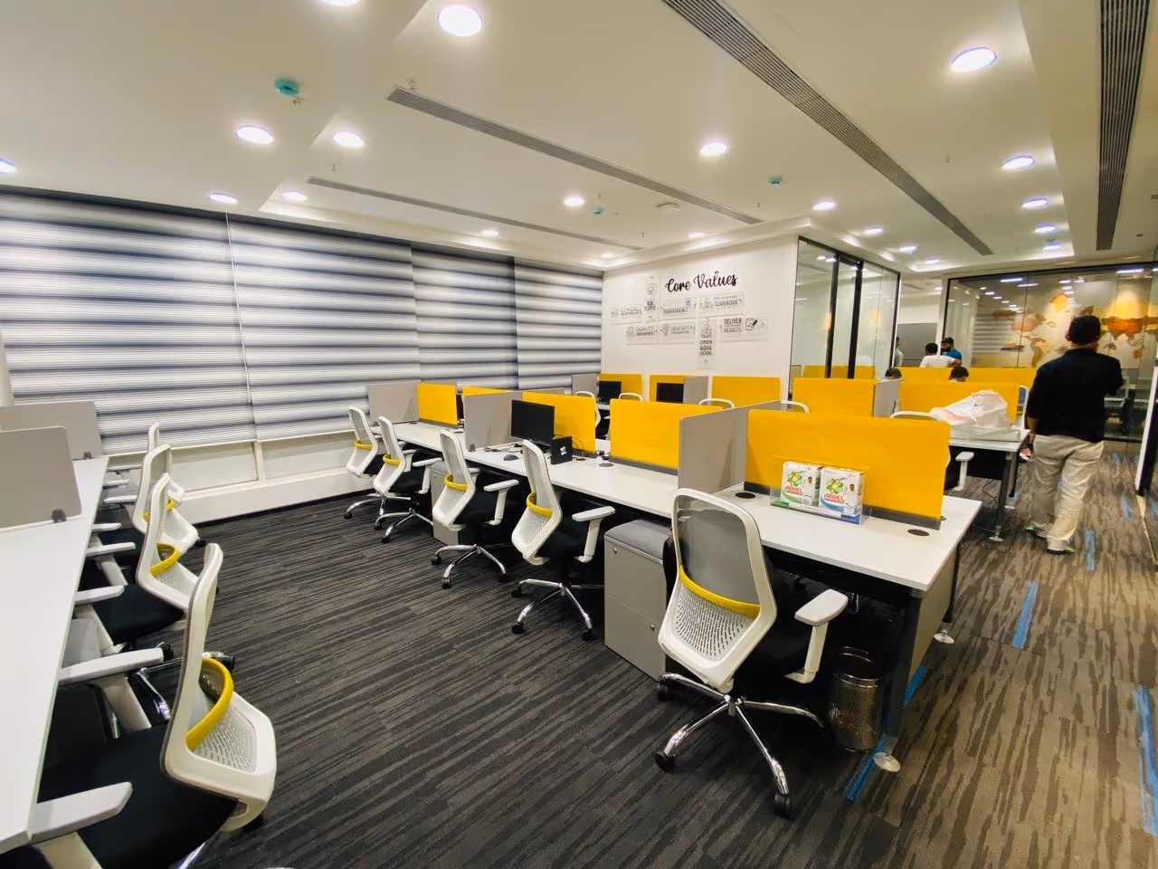 Open-plan office workstations with white desks and yellow privacy screens.