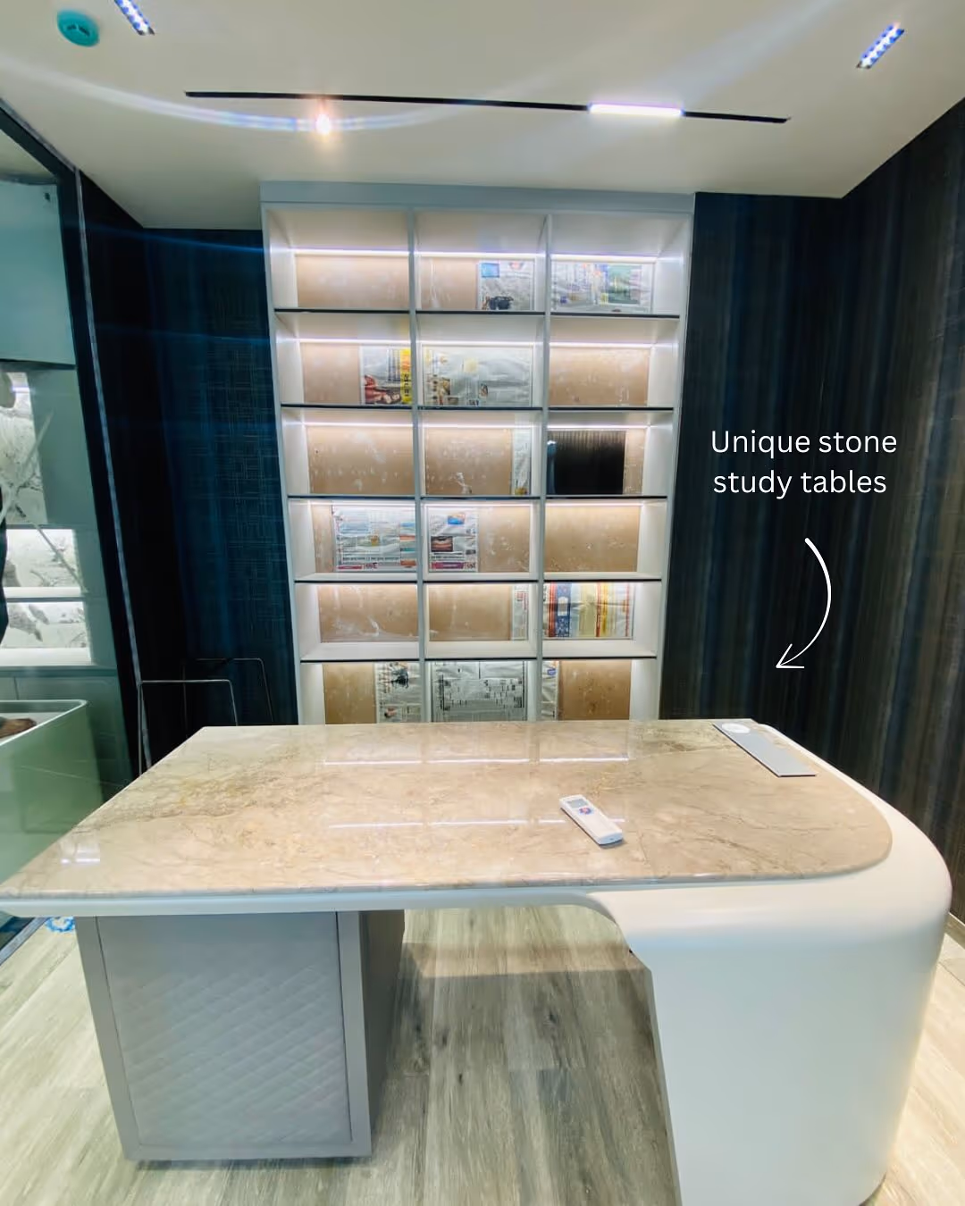 A wide luxury home office desk with a burl-wood top and slim brass legs, set against a fitted wall of shelving.