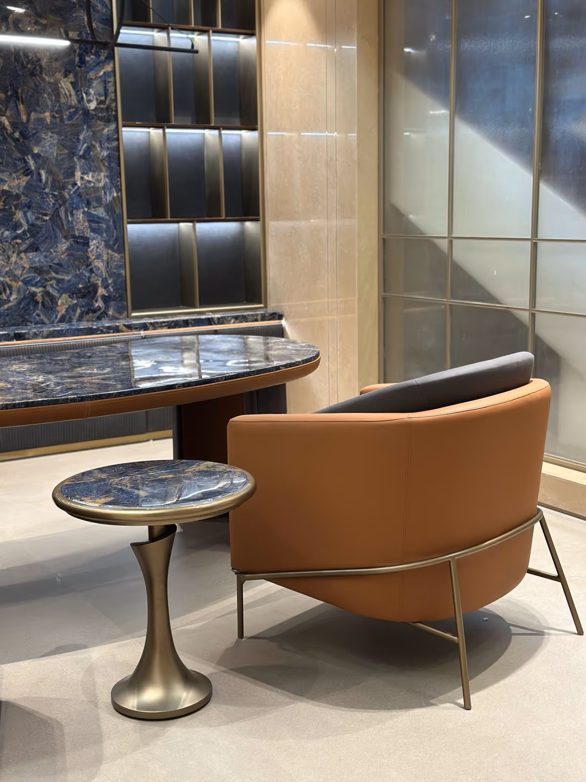 A quiet meeting corner in a CEO cabin with two leather lounge chairs, a low stone table, a rug and a soft floor lamp by a window.