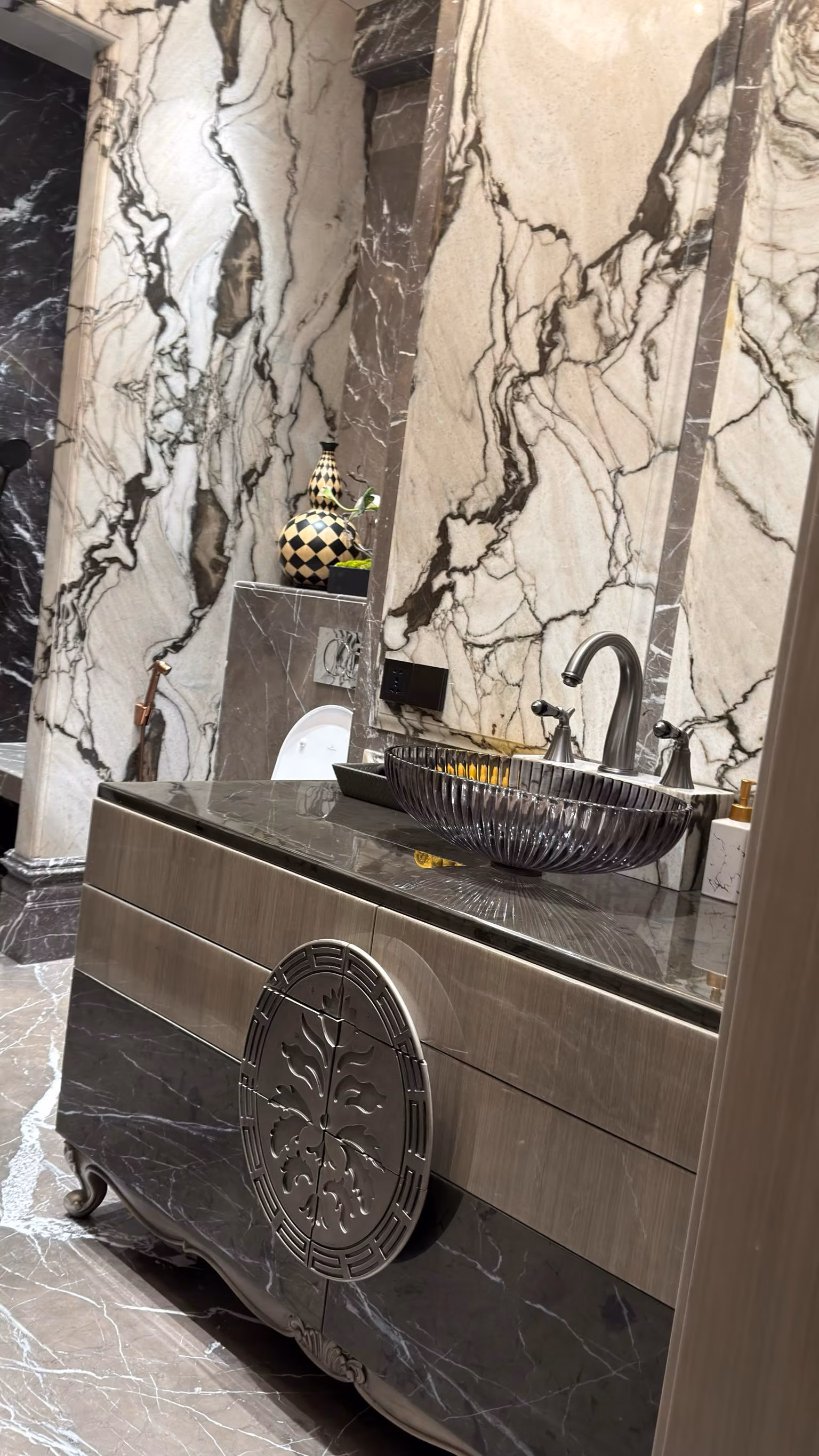 Carved marble bathroom vanity with a mosaic vessel sink against a book-matched marble wall