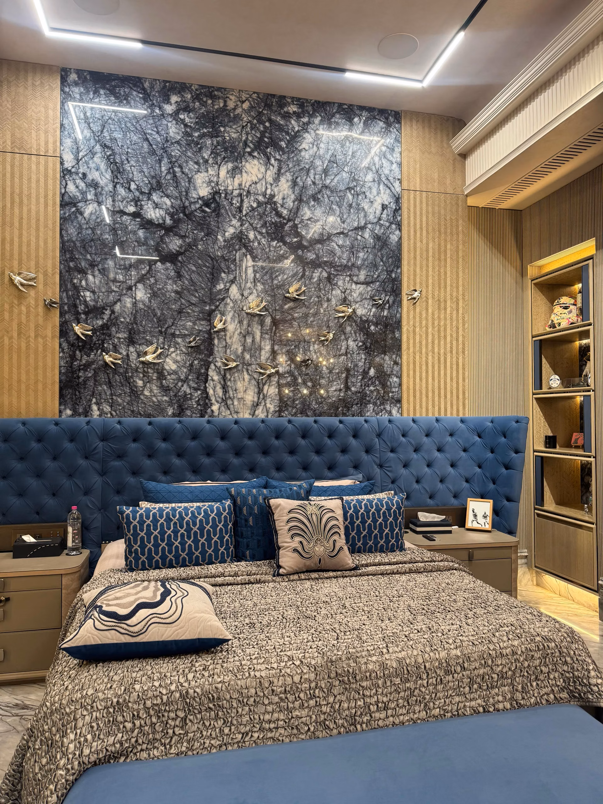 Blue button-tufted headboard bed against a dark marble feature wall with a fitted wardrobe in a luxury bedroom