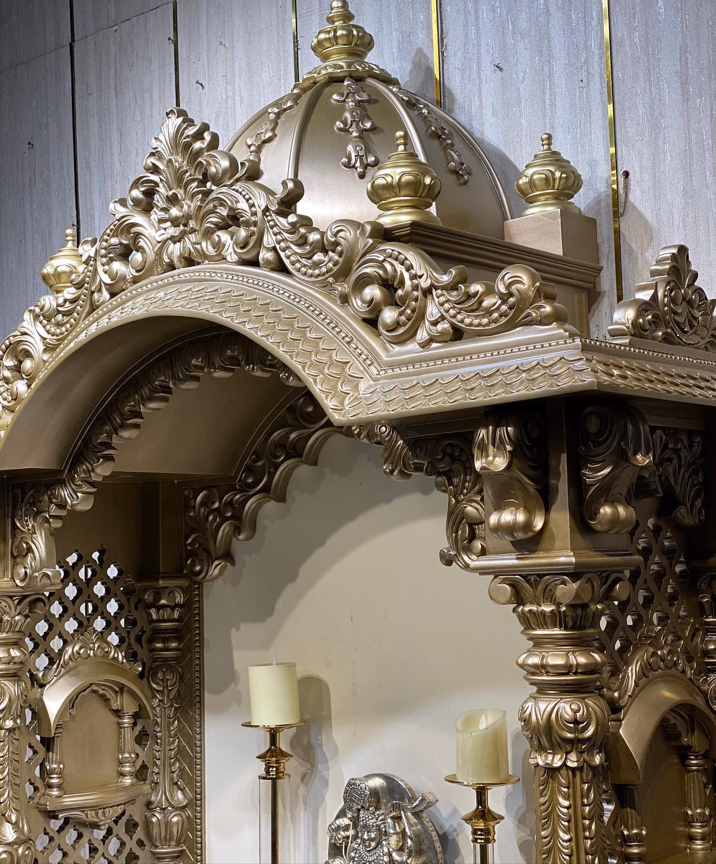 Close detail of the mandir canopy showing the carved dome, kalash finials, layered scroll brackets and the beaded arch band worked into solid timber.