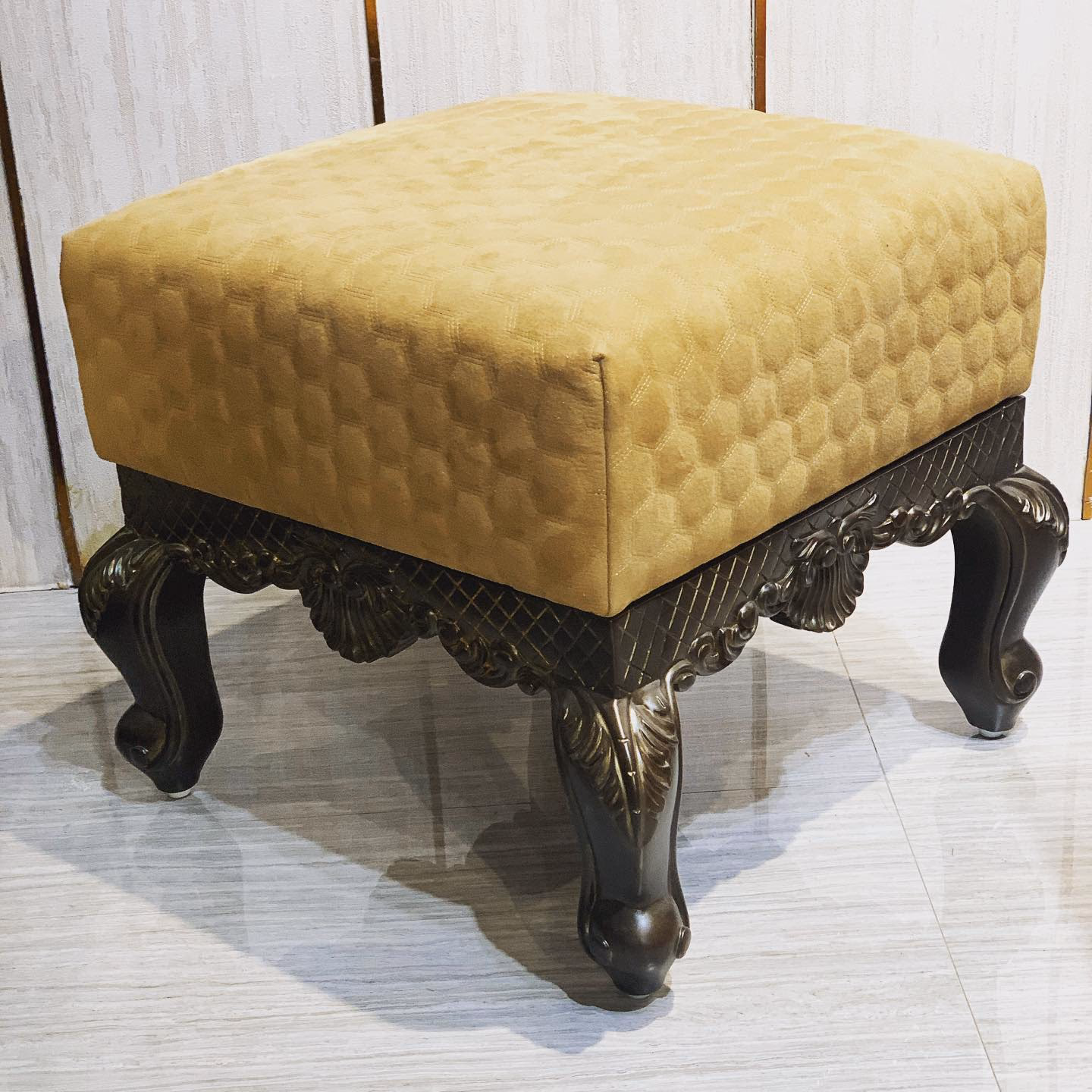 Square pooja room stool with a gold honeycomb-quilted velvet top on a hand-carved dark wood frame with shell motifs, lattice apron and cabriole legs ending in scrolled feet.