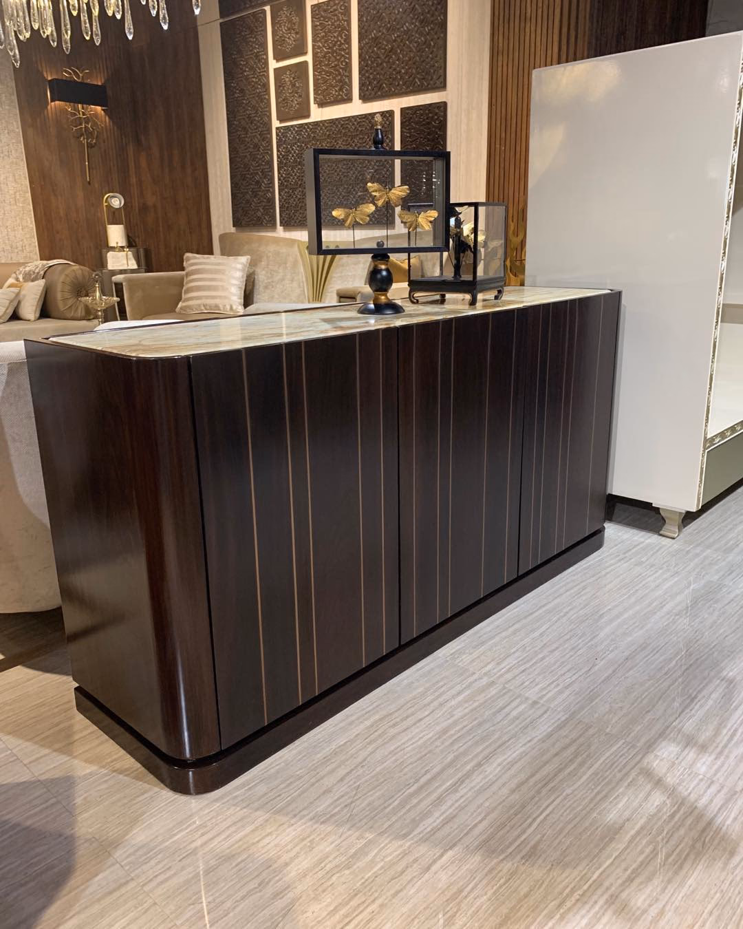 Three-door shoe cabinet in high-gloss ebony with fine brass inlay lines running down each fluted door, a curved end panel, a golden onyx top and a recessed plinth.