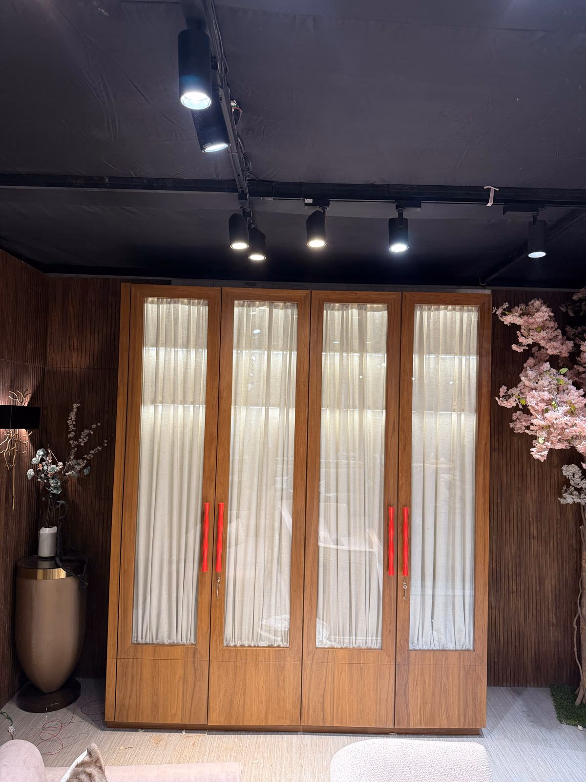 Four-door wood wardrobe with sheer curtain-lined glass panels and sculpted red wood handles.