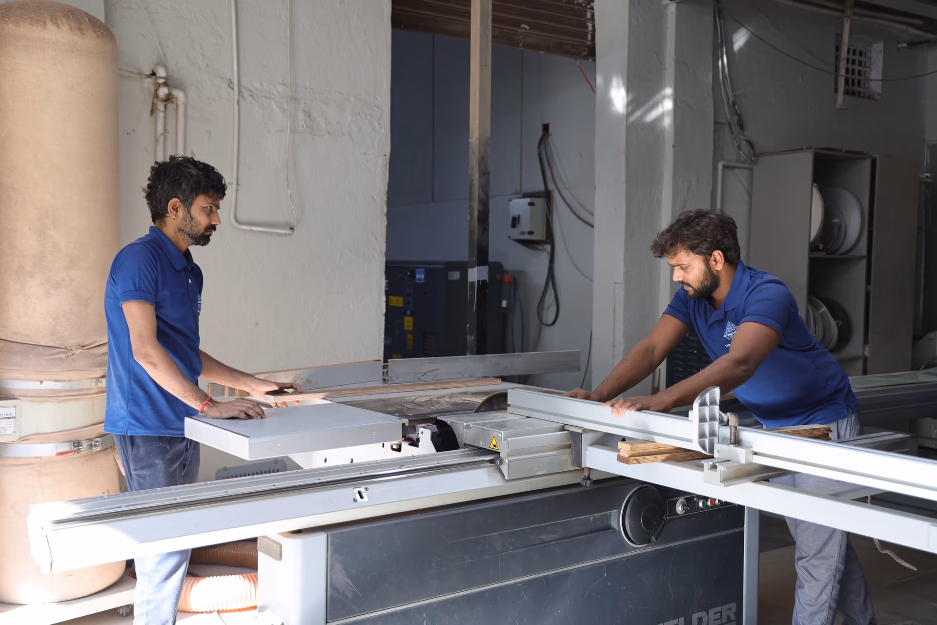 Factory craftsmen guiding a large panel through a precision panel saw in a furniture factory.