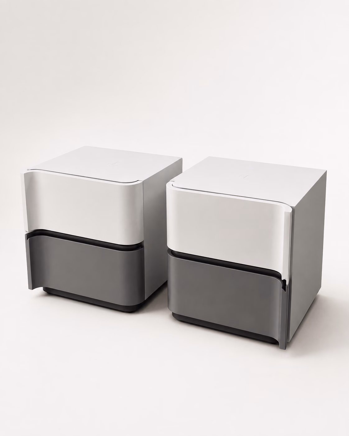 A pair of Designatore cube bedside tables shown alone on a white ground, each with a soft ivory upper drawer over a warm grey lower drawer, softly curved handleless fronts, a dark recessed shadow gap between them and a recessed plinth.