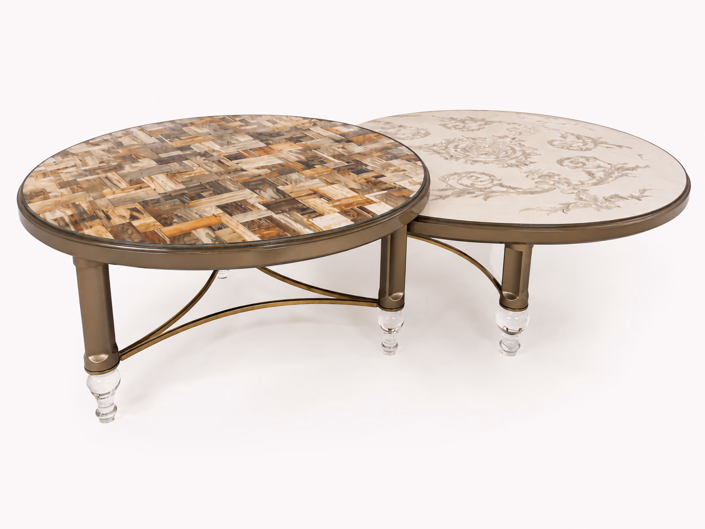 A Designatore nesting pair of round centre tables shown alone on a bone ground, one topped with a geometric natural stone inlay in warm earthy tones and one with a floral stone inlay on a cream base, both on champagne bronze metal frames with curved stretchers and clear crystal feet.