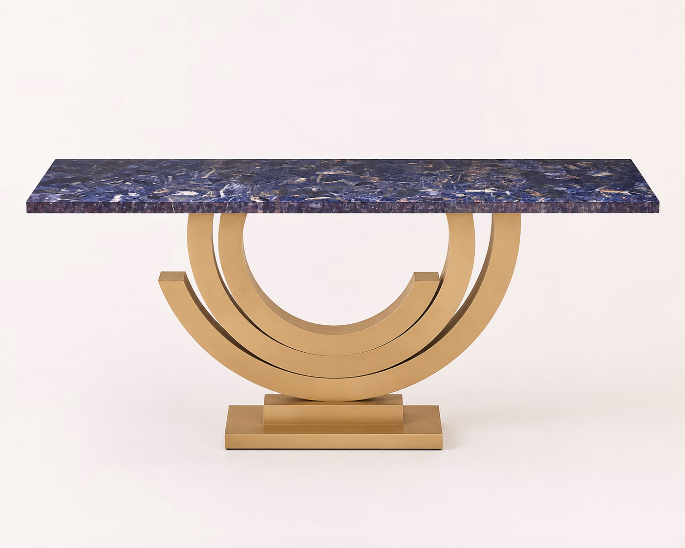 Designatore console table shown alone on a bone ground, with a thick deep blue Blue Soda Light semi-precious stone slab top and a sculptural brushed gold metal base formed as nested arcs on a layered rectangular plinth.