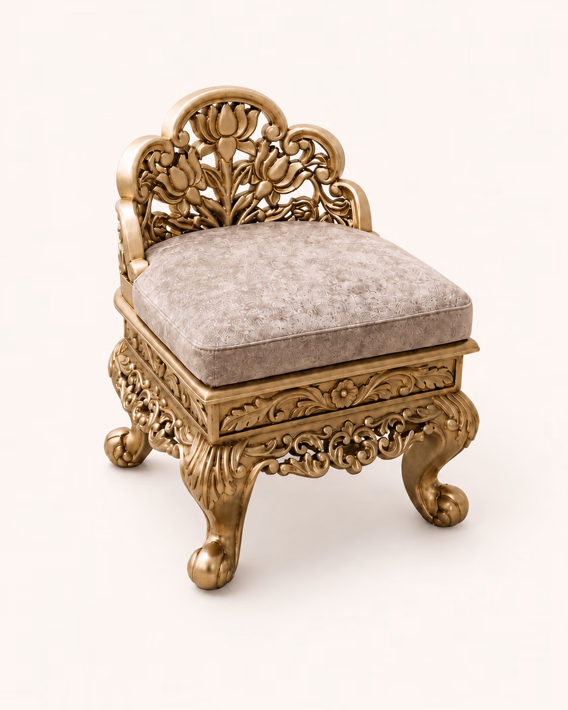 Designatore low pooja chowki chair shown alone on a bone ground, hand-carved in solid wood with a pierced lotus and tulip crest, scrolled arms, a carved apron, cabriole legs with ball feet and a grey floral-embossed cushioned seat, all in a soft gold finish.