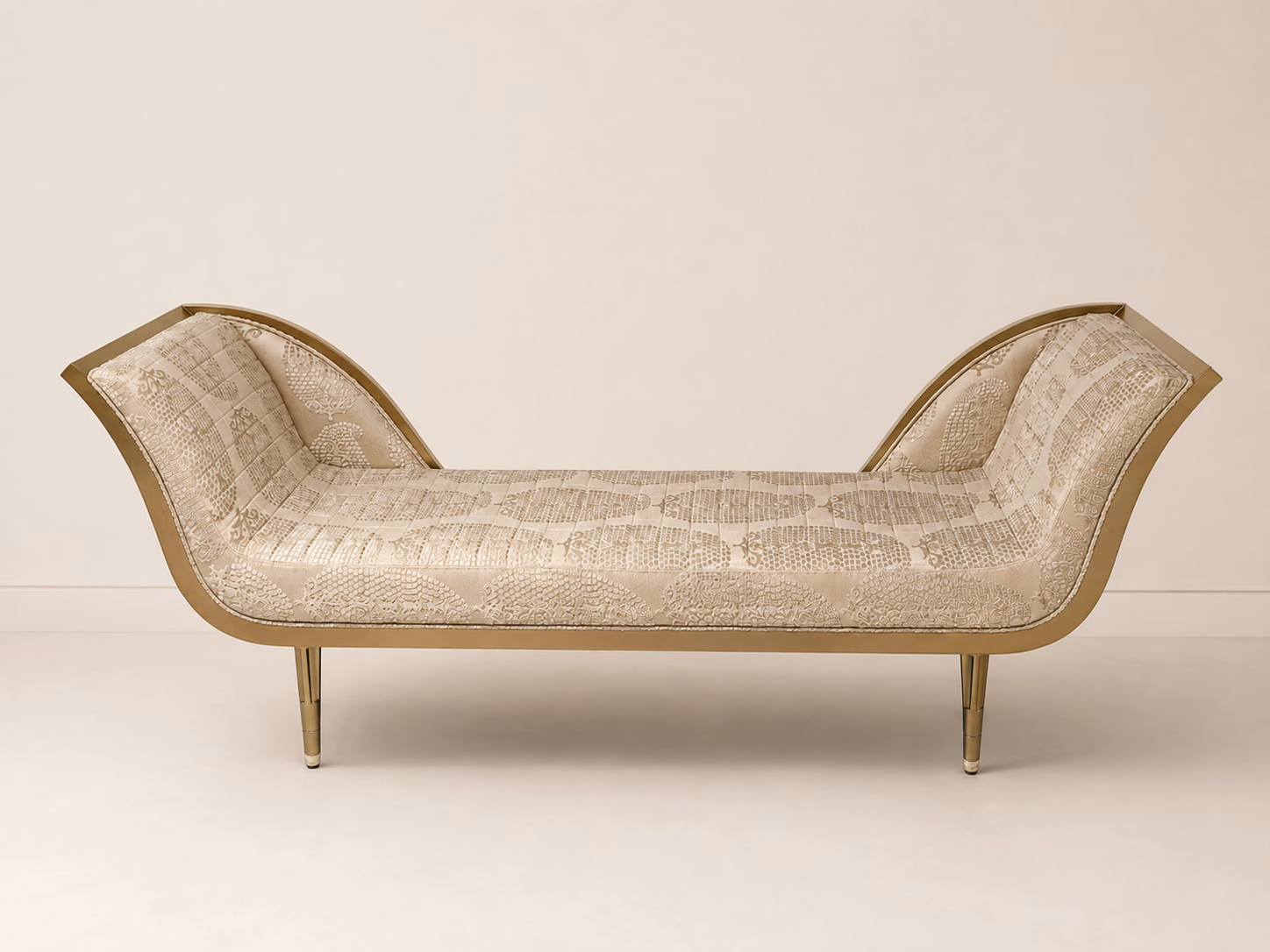 Designatore chaise bench shown alone on a bone ground, with both ends curving upward, upholstered in a softly patterned beige jacquard with precision piping, held in a brushed champagne gold metal frame on slim tapered legs with stone-finished feet.