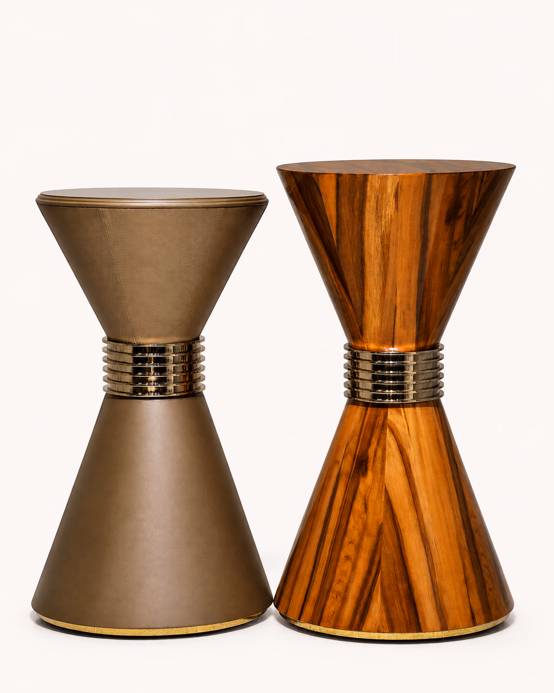 A pair of Designatore hourglass drum side tables shown alone on a bone-white ground, one wrapped in matte taupe leather and one in high-polish solid wood, each cinched at the waist by a stacked polished metal collar over a brass base trim.