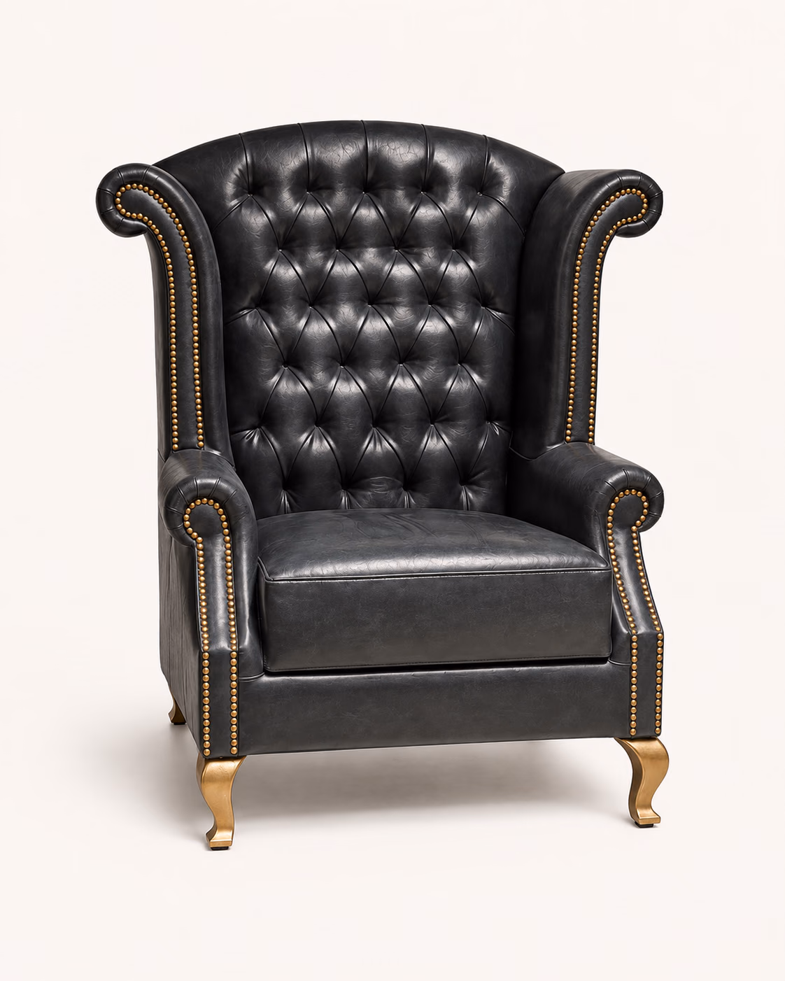 Designatore wing chair shown alone on a bone-white ground, upholstered in black full-grain leather with a deep diamond-buttoned back, tall wings, scrolled arms outlined in hand-applied brass nailheads, a single tailored seat cushion and sculpted gold cabriole legs.